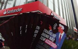 Foto mostra o folder sobre o novo canal de denúncias, onde se lê ""Trabalho dogno não tem assédio", diante da fachada da Torre Santander