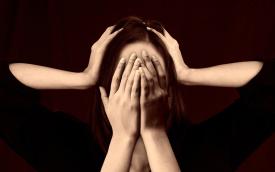 Imagem de uma mulher, com as mãos cobrindo o rosto e os ouvidos, remetendo a sofrimento mental