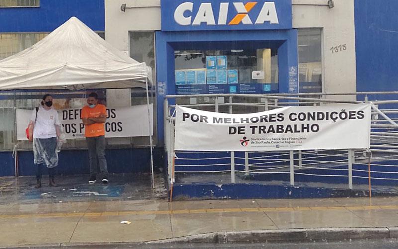 Foto mostra fachada de agência da Caixa Econômica Federal em Sapopemba que foi palco de protesto para cobrar conserto de ar-condicionado. Em frente à fachada está estendida uma faixa escrita: "Por melhores condições de trabalho" Fachada de agência da Caixa Econômica Federal em Sapopemba que foi palco de protesto para cobrar conserto de ar-condicionado