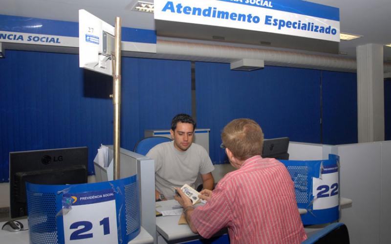 Servidor do INSS atende pensionista ao lado de um guichê vazio