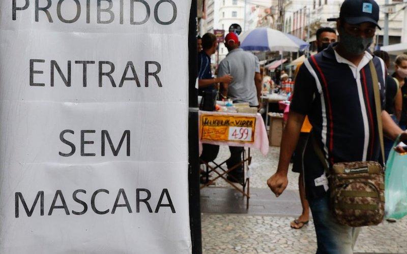 Foto: Fernando Frazão/Agência Brasil Homem de máscara passando ao lado de um cartaz com a frase "proibido entrar em máscara"