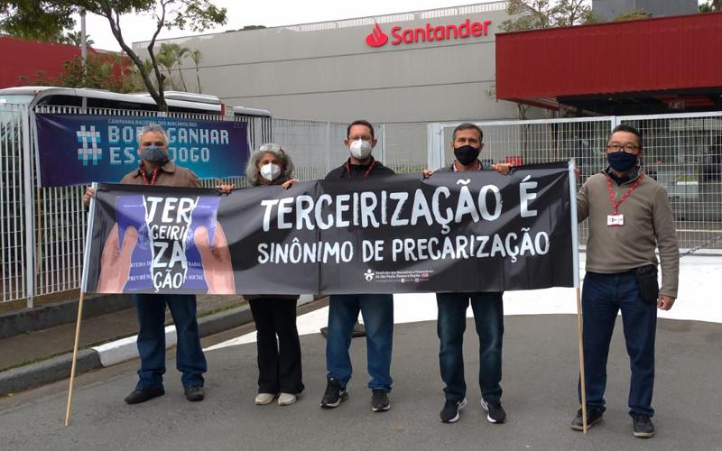 Os dirigentes sindicais Roberto Paulino, Vera Marchioni, José Roberto Santana, Wagner Cabanal e Cassio Murakami em frente a F1RST durante protesto contra a terceirização Os dirigentes sindicais Roberto Paulino, Vera Marchioni, José Roberto Santana, Wagner Cabanal e Cassio Murakami em frente a F1RST durante protesto contra a terceirização. Eles seguram uma faixa escrita "Terceirização, sinônimo de precarização"