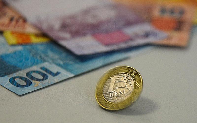 Duas propostas estão em debate na sociedade. Uma prevê apenas a simplificação de impostos existentes, enquanto outra busca justiça fiscal e progressividade na arrecadação Cédulas de 100, 20, 5 e 10 reais sobrepostas ao fundo e uma moeda de um real no primeiro plano
