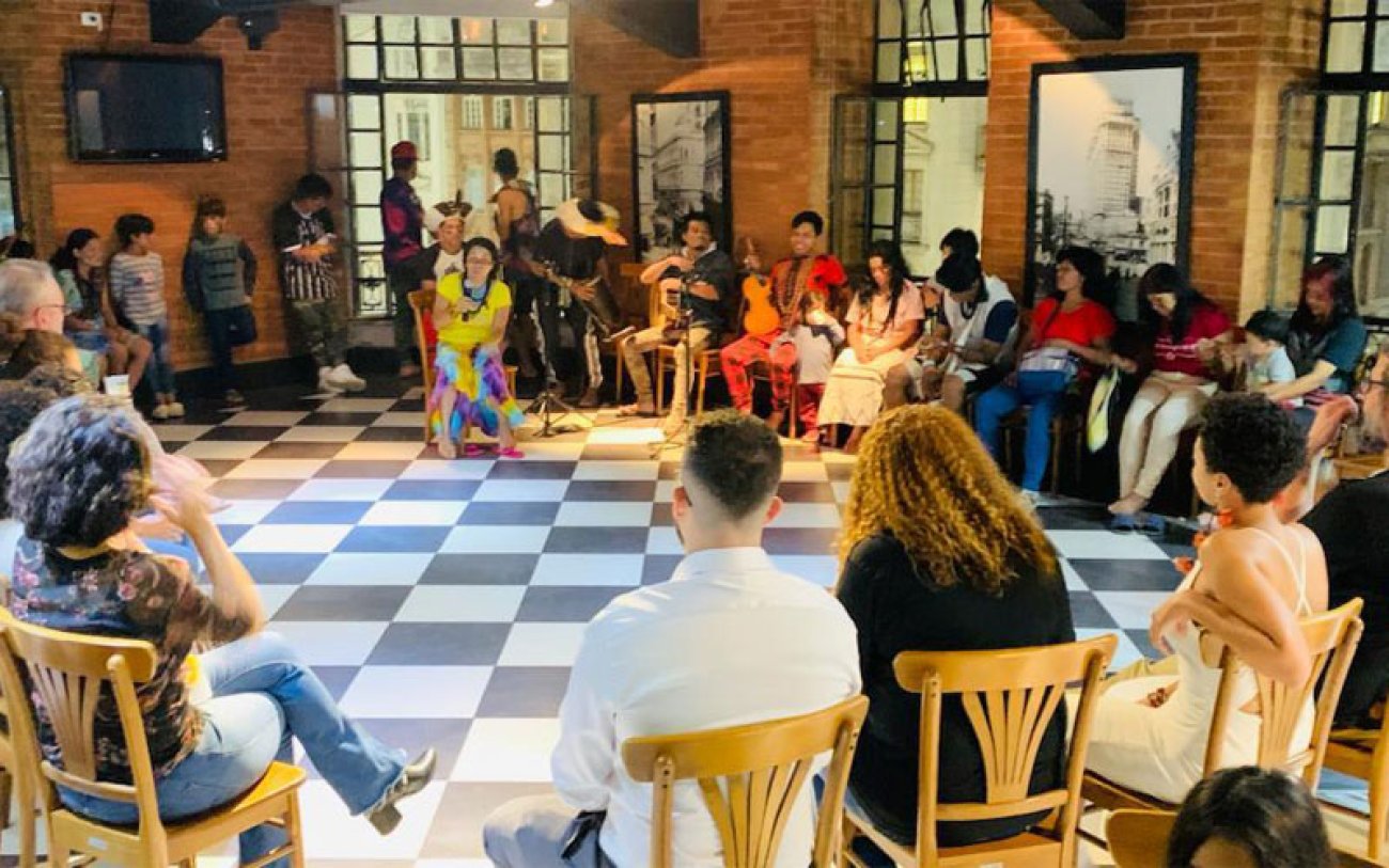 Pessoas ouvem a liderança indígena Laura Araievoty, da comunidade indígena Tekoa Tapemirim/Barragem, na Terra Indígena Tenondé Porã, em Paralheiros, durante a terceira edição do Samba no Café Imagem mostra pessoas reunidas durante a terceira edição do Samba no Café