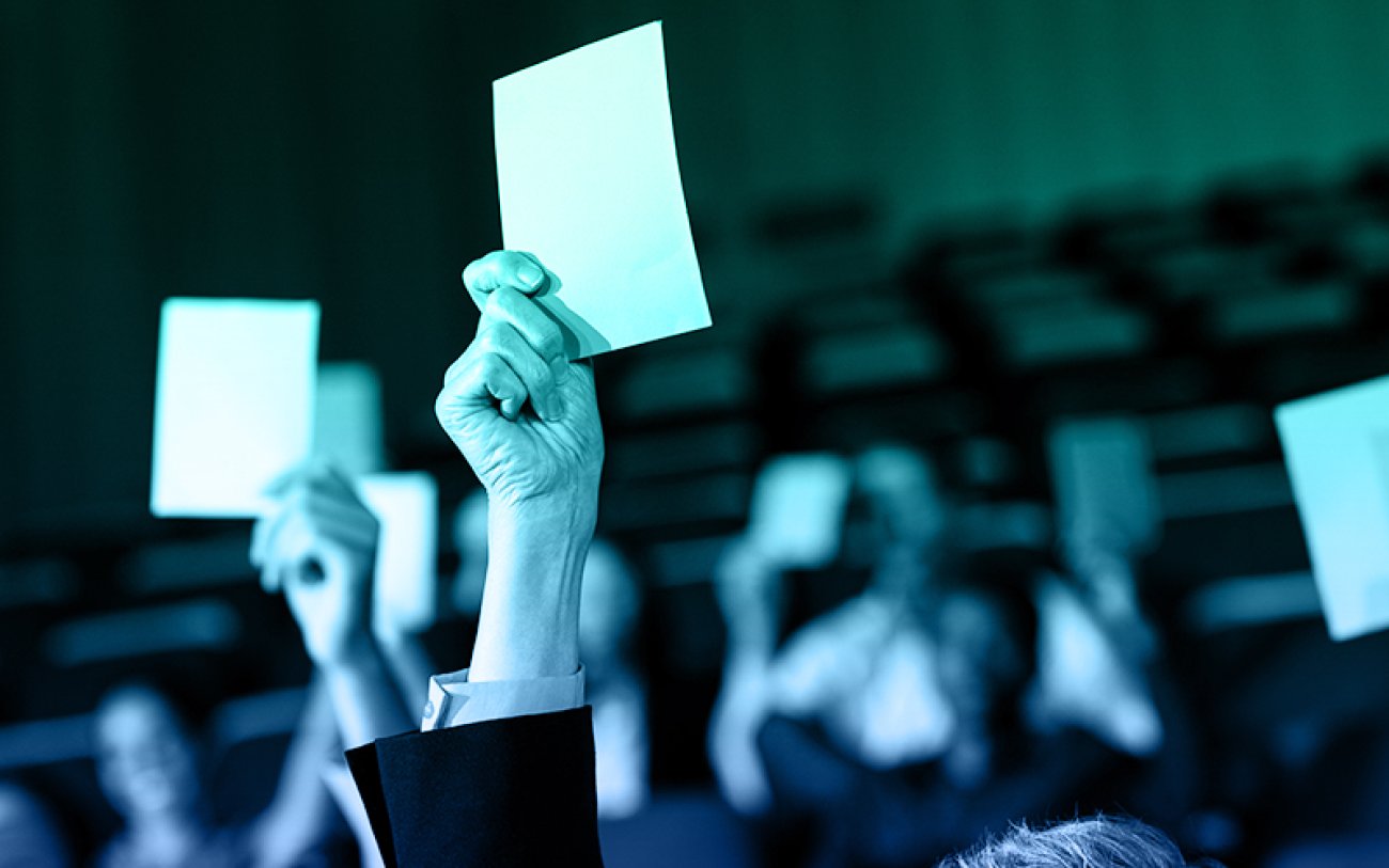 Imagem onde se vêem mãos levantando crachás de votação