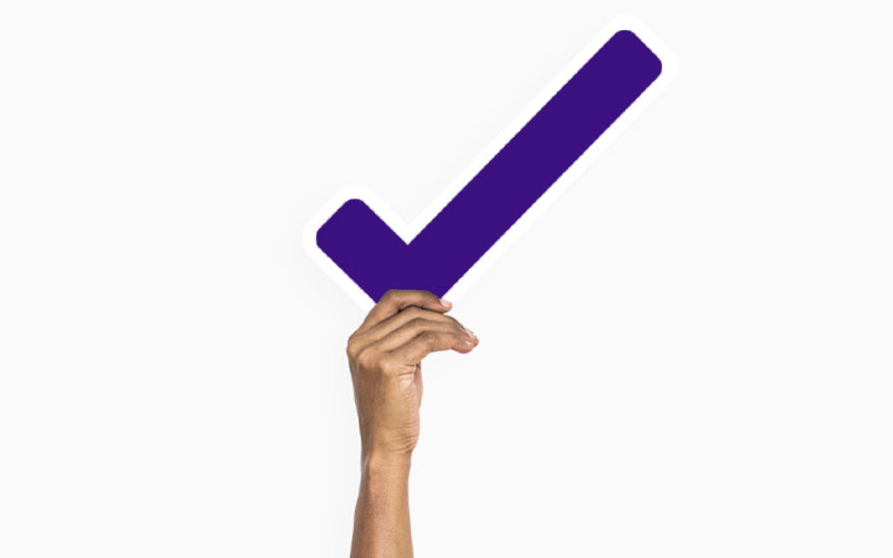 Imagem com fundo brando e uma mão segurando um sinal de "check", indicando aprovação