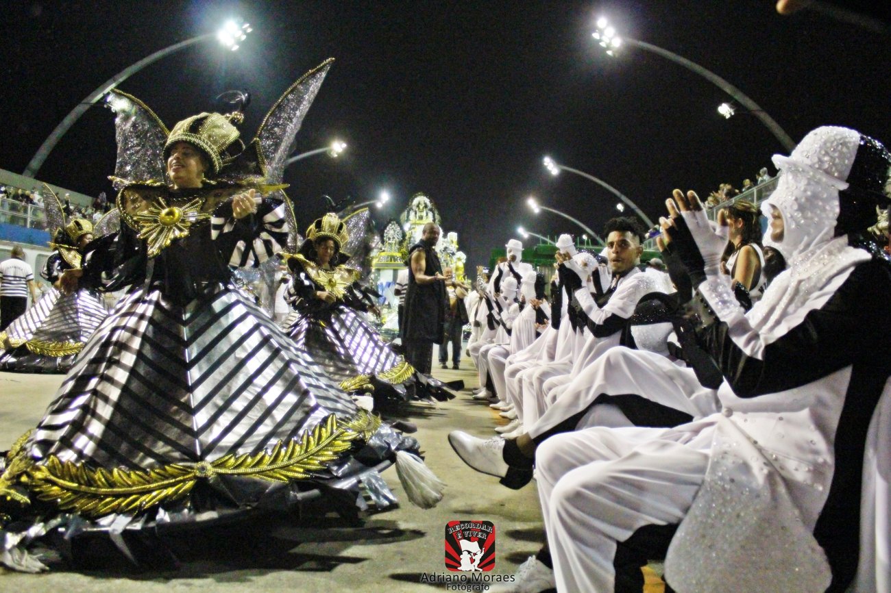 Integrantes da escola de samba Vai-Vai durante o desfile da escola em 2024 Fotografia mostra integrantes fantasiados de preto e branco ajoelhados ao lado de uma porta-bandeira da Vai-Vai