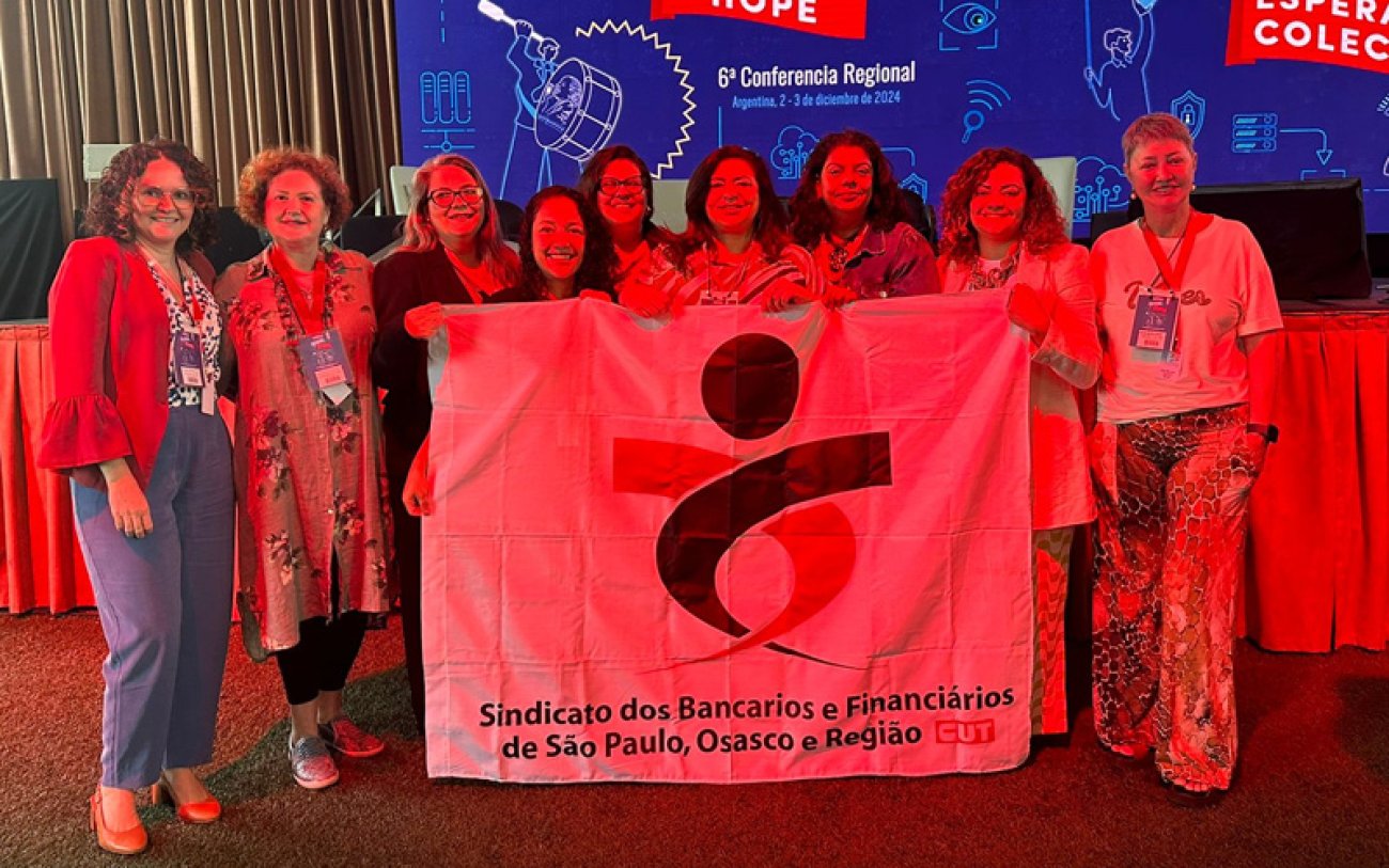 Delegação da Contraf-CUT representa os bancários brasileiros nos encontros que visam organizar a luta coletiva dos trabalhadores do continente (foto: Seeb-SP) Dirigentes do Sindicato e da Contraf-CUT posam para foto segurando bandeira com a logo do Sindicato, em Conferência da UNI Américas