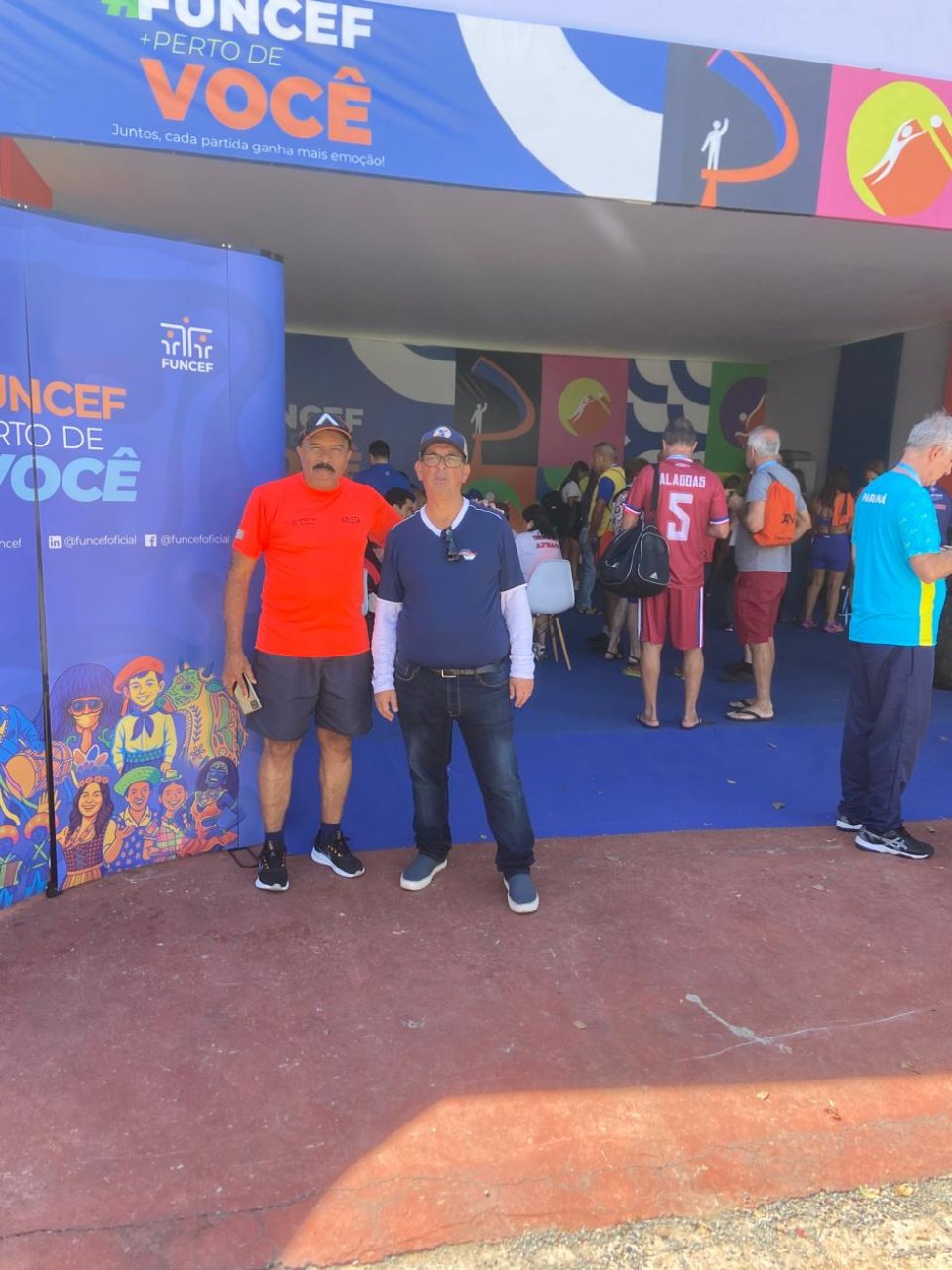 Dirigentes Kardec de Jesus e Valter San Martin nos XIV Jogos da Fenacef 2025 Fotografia mostra dois homens com roupas esportivas nas cores vermelho, azul e branco