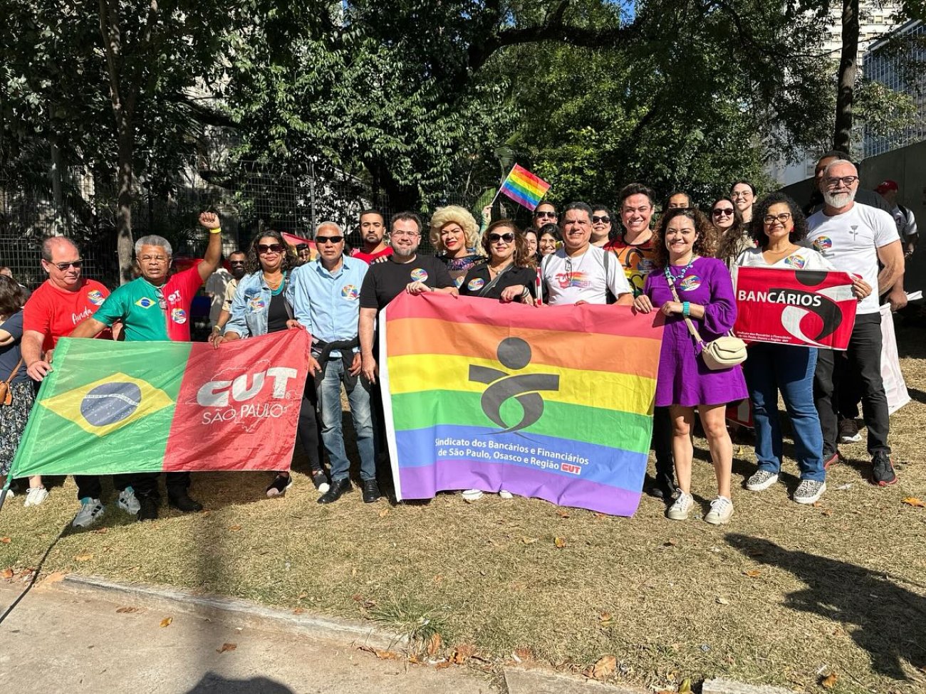 Bancários marcam presença na 1ª Marcha LGBT+ organizada pela CUT Fotografia tem pessoas segurando faixa com as cores do arco-iris