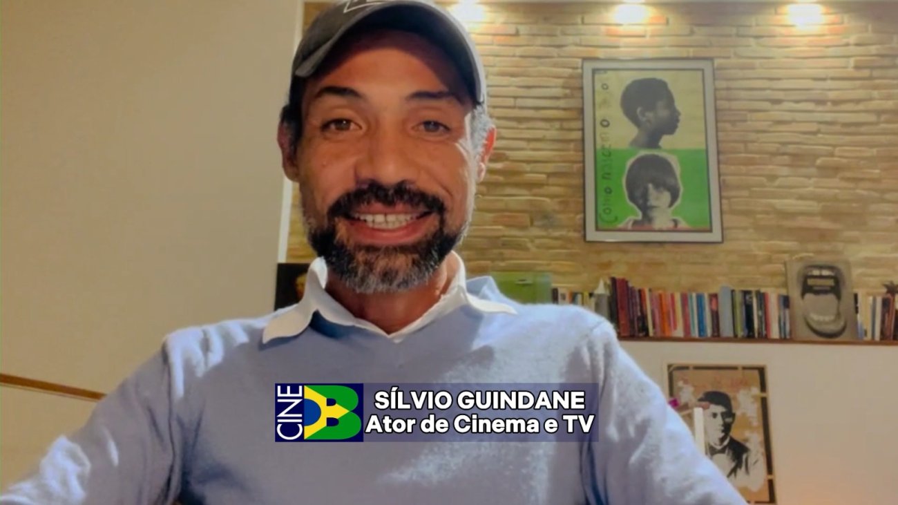 Ator Silvio Guindane fala sobre o 9º Prêmio do CineB Homem sentado, de pele negra e bone, vestindo camisa azul clara