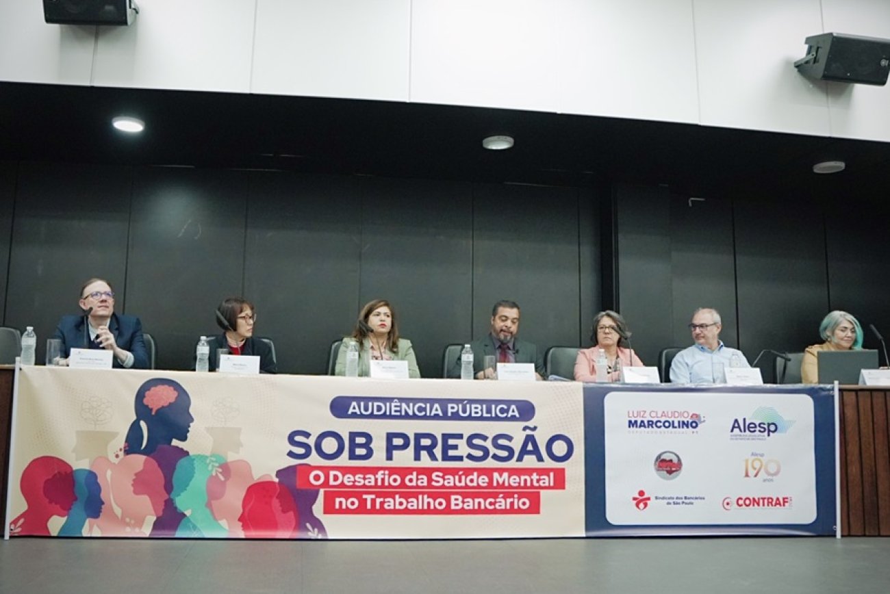 A partir da esquerda, Patrick Maia Merísio Procurador do Trabalho; Maria Maeno, médica e pesquisadora da Fundacentro; Neiva Ribeiro, presidenta do Seeb-SP; Luiz Cláudio Marcolino, deputado estadual; Maria Leonor Poço Jakobsen, advogada especialista em direitos humanos; e Ana Lúcia Ramos, secretária-geral da Fetec-CUT/SP Imagem mostra mesa da audiência pública “Sob Pressão: O Desafio da Saúde Mental no Trabalho Bancário” estão lado a lado na mesa, Patrick Maia Merísio Procurador do Trabalho; Maria Maeno, médica e pesquisadora da Fundacentro; Neiva Ribeiro, presidenta do Seeb-SP; Luiz Cláudio Marcolino, deputado estadual; Maria Leonor Poço Jakobsen, advogada especialista em direitos humanos; e Ana Lúcia Ramos, secretária-geral da Fetec-CUT/SP.