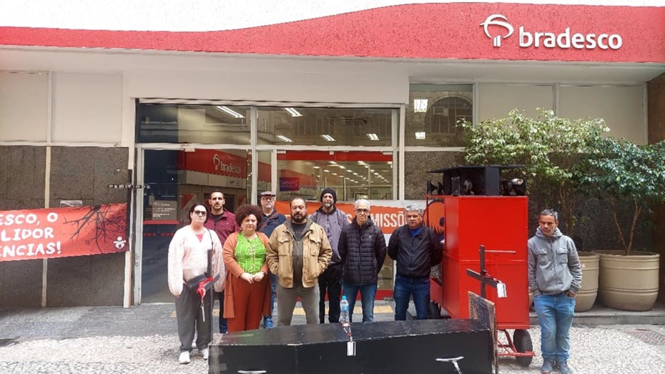 Imagem mostra dirigentes sindicais enfileirado em frente a uma agência do Bradesco. na frente deles, um caixão representando a morte dos empregos bancários e das agências