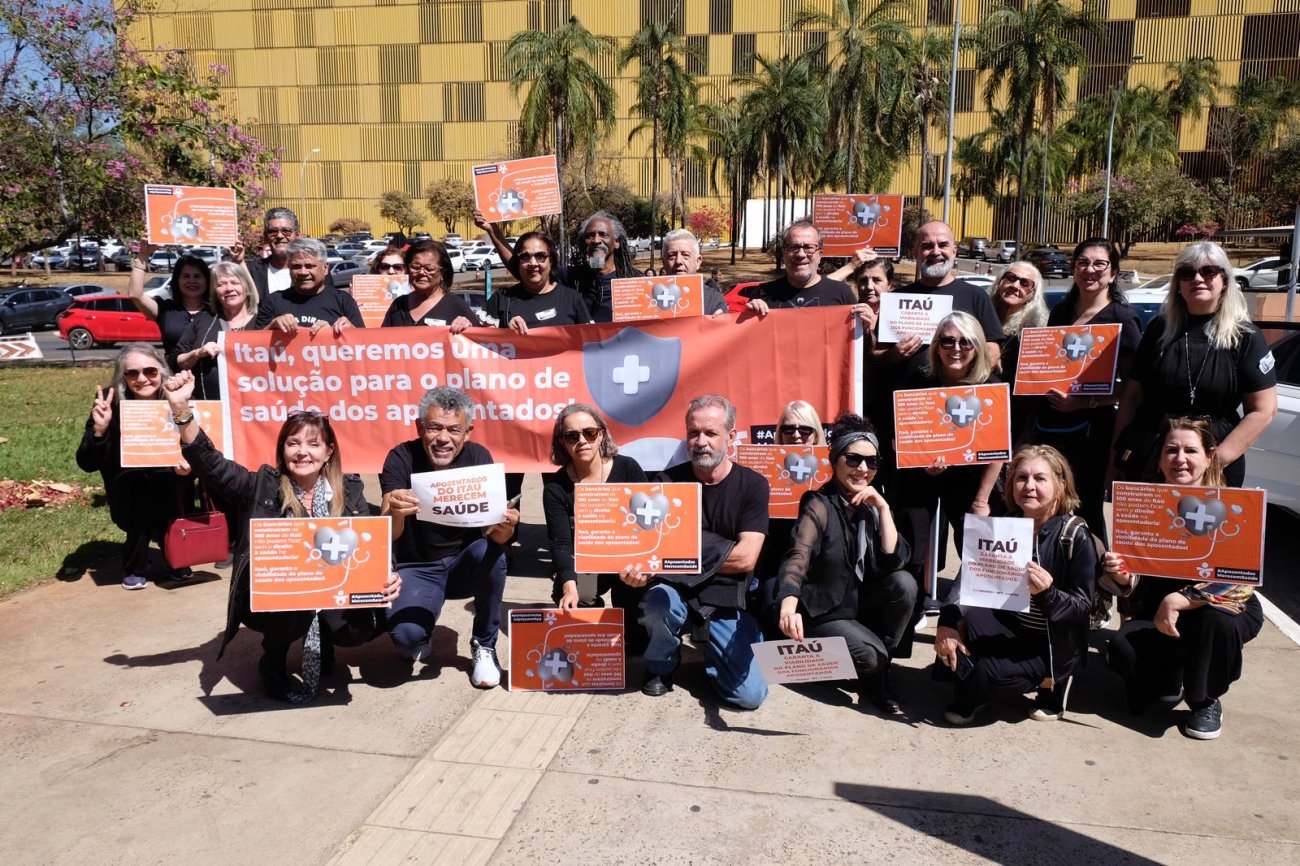 Imagem mostra aposentados do Itaú segurando cartazes em frente antes da audiência pública para debater os valores das mensalidades do plano de saúde dos ex-funcionários do banco
