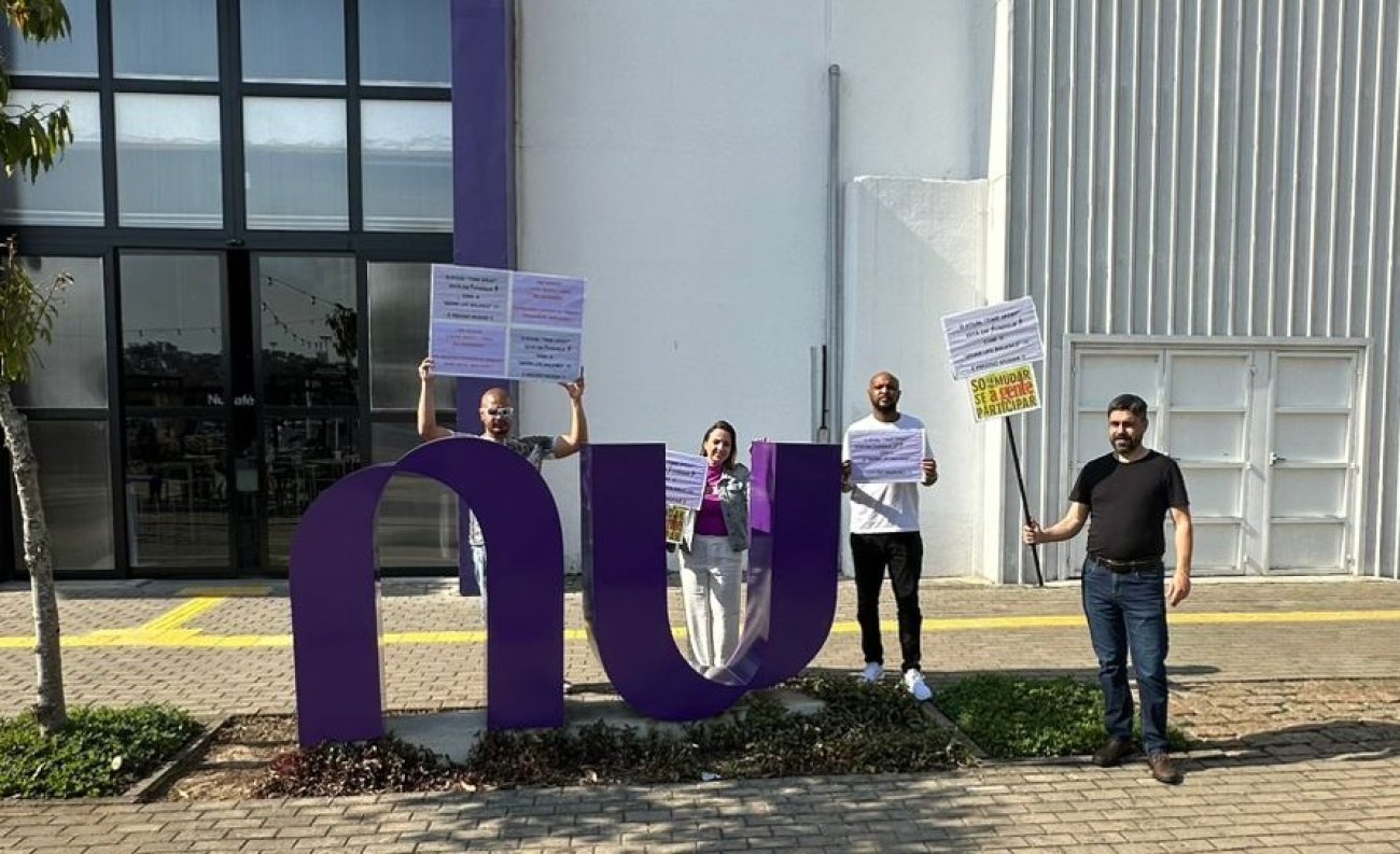 Imagem mostra dirigentes em frente ao prédio do Nubank. Eles seguram placas