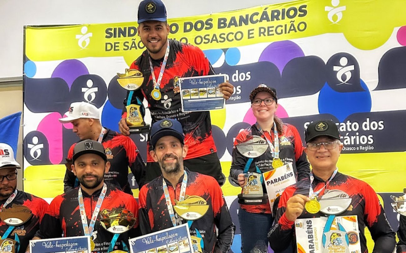 Torneio de Pesca em trio sucesso entre os bancários Fotografia mostra participantes do torneio de pesca com camisa colorida de vermelha, amarelo e preto segurando troféu nas mãos