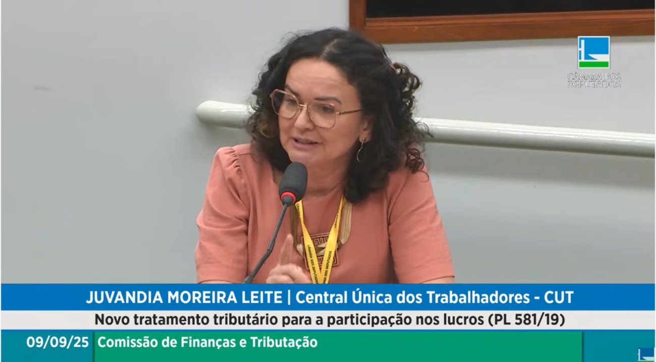 imagem mostra juvandia moreira durante audiência pública sobre rojeto de Lei que dá à PLR o mesmo tratamento fiscal conferido aos lucros ou dividendos distribuídos aos sócios ou acionistas de empresas. Ela é uma mulher branca, de cabelos ngros e levemente encaracolados, cortados na altura dos ombros. ela usa uma blusa rosa