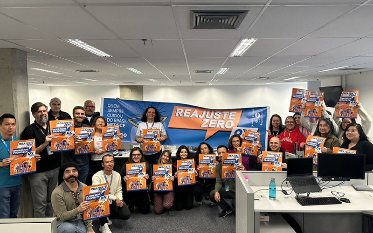 Imagem mostra empregados da Caixa lado a lado portando cartazes onde se lê "reajuste zero. Queremos proposta!"