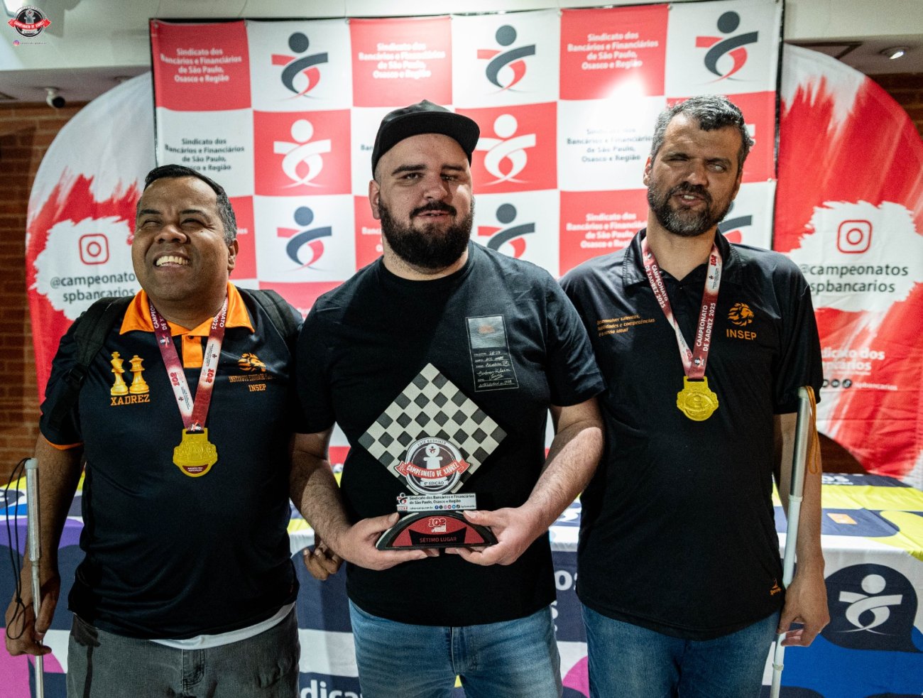 Atletas cegos destaque neste Campeonato de xadrez dos bancários foto: SEEB-SP fotografia mostra 3 homens brancos cegos, com camisa preta, um deles boné e medalha de participação no peito