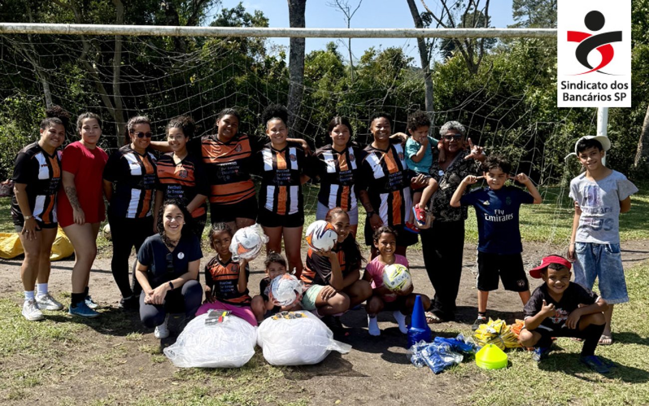 Foto: Divulgação Fotografia do tipo feminino de futebol de várzea, posando em frente à trave, com logo do Sindicato aplicada no canto superior direito da imagem.