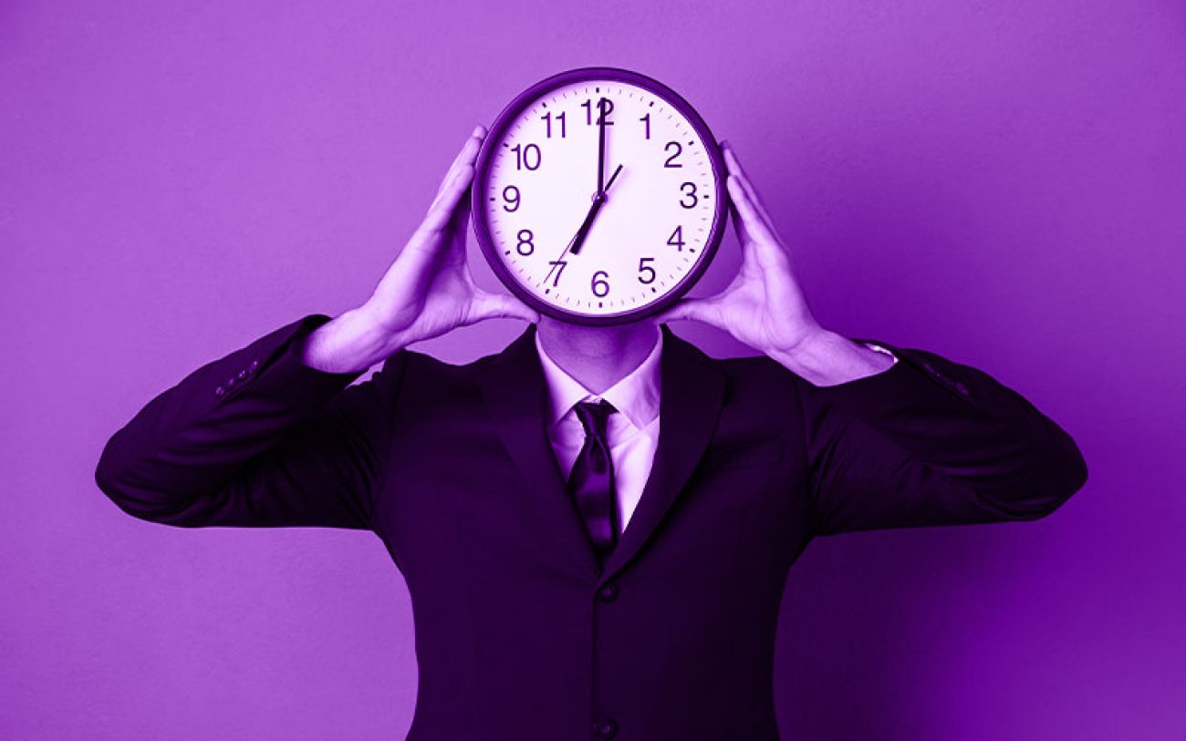 Imagem: Freepik Imagem de um homem de terno, segurando um relógio na frente do seu rosto, em fundo roxo