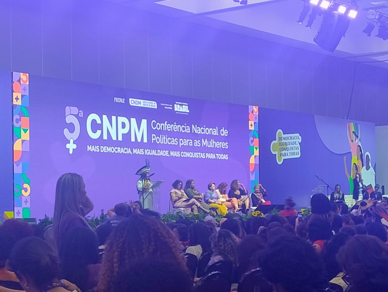 Sonia Guajajara, Ministra dos Povos Indígenas do Brasil, discursa durante a 5ª Conferência Nacional de Políticas para as Mulheres Imagem mostra plenário da 5ª conferencia nacional de política para as mulheres. a imagem foca o palco do evento enquanto discursa Sonia Guajajara, Ministra dos Povos Indígenas do Brasil