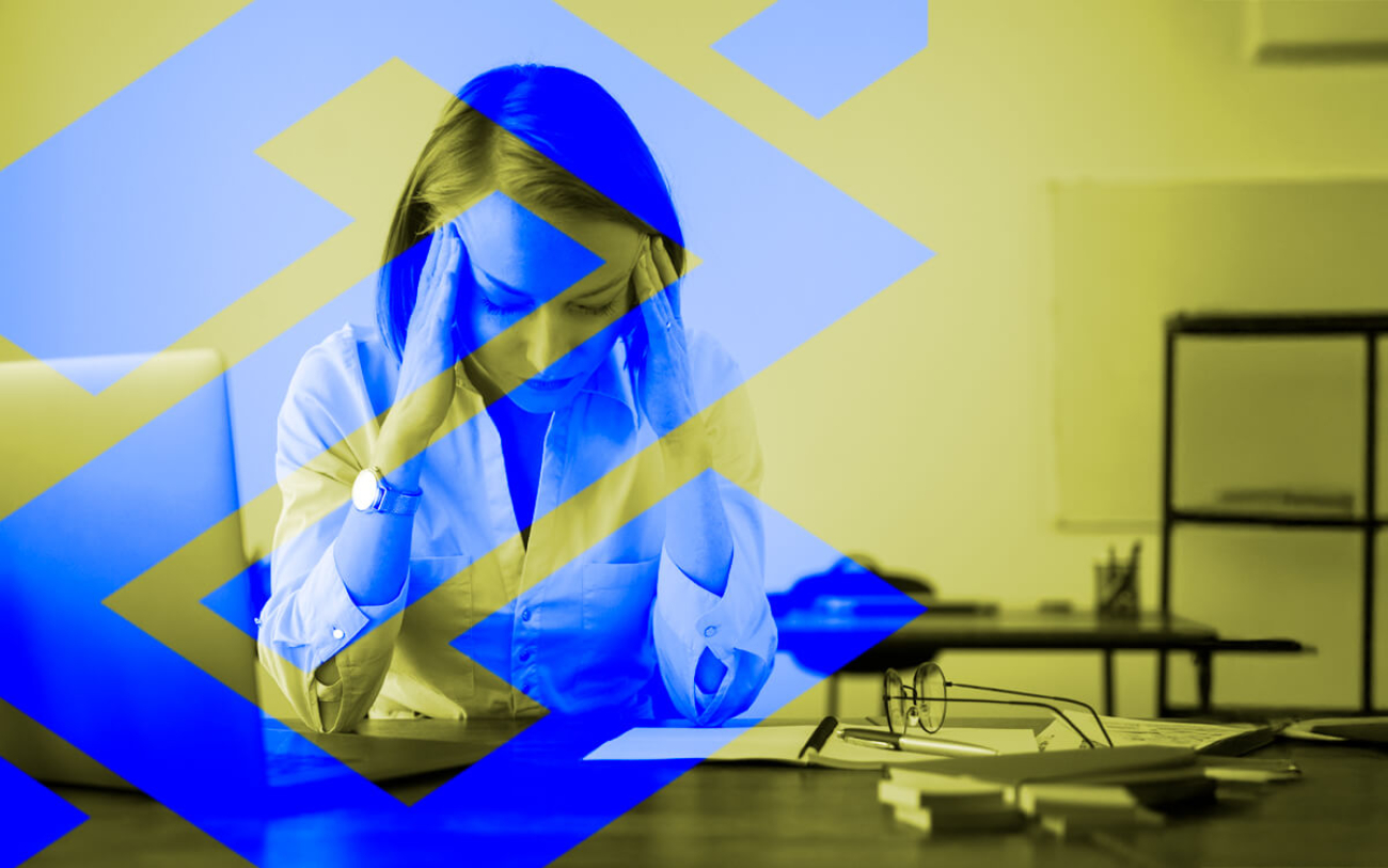 Arte mostra uma mulher de cabeiça baixa e aparentando preocupação sobre uma mesa de trabalho