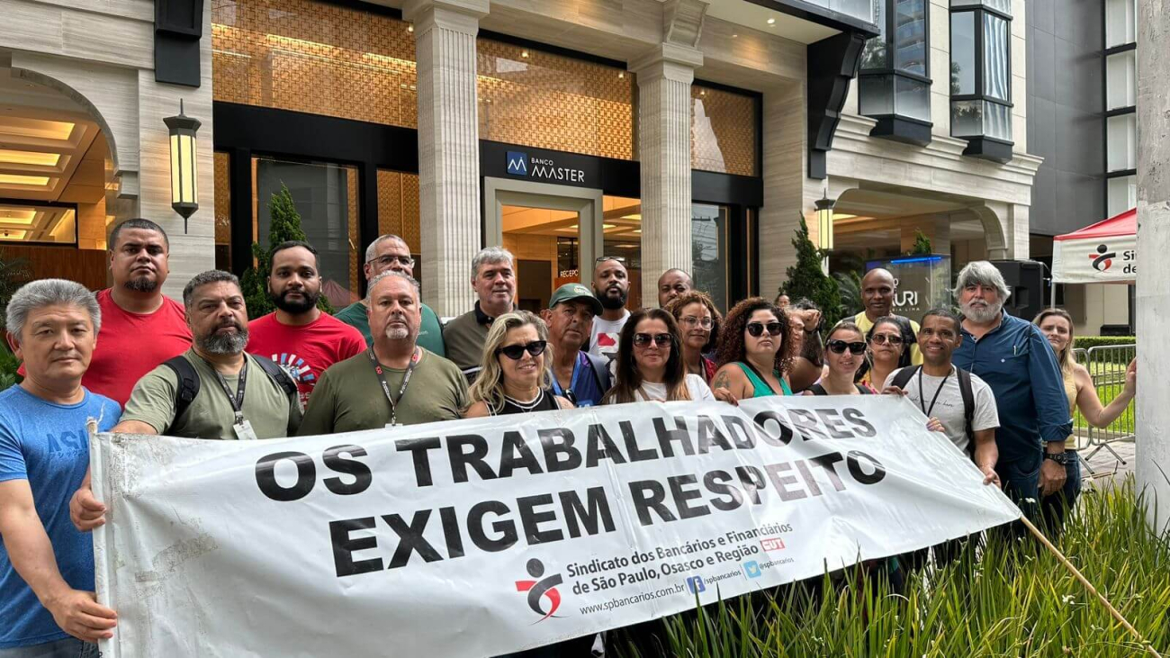 Imagem mostra dirigentes do Sindicato dos Bancários em frente à porta do Banco Master, portanto uma faixa onde se lê "os trabalhadores exigem respeito"