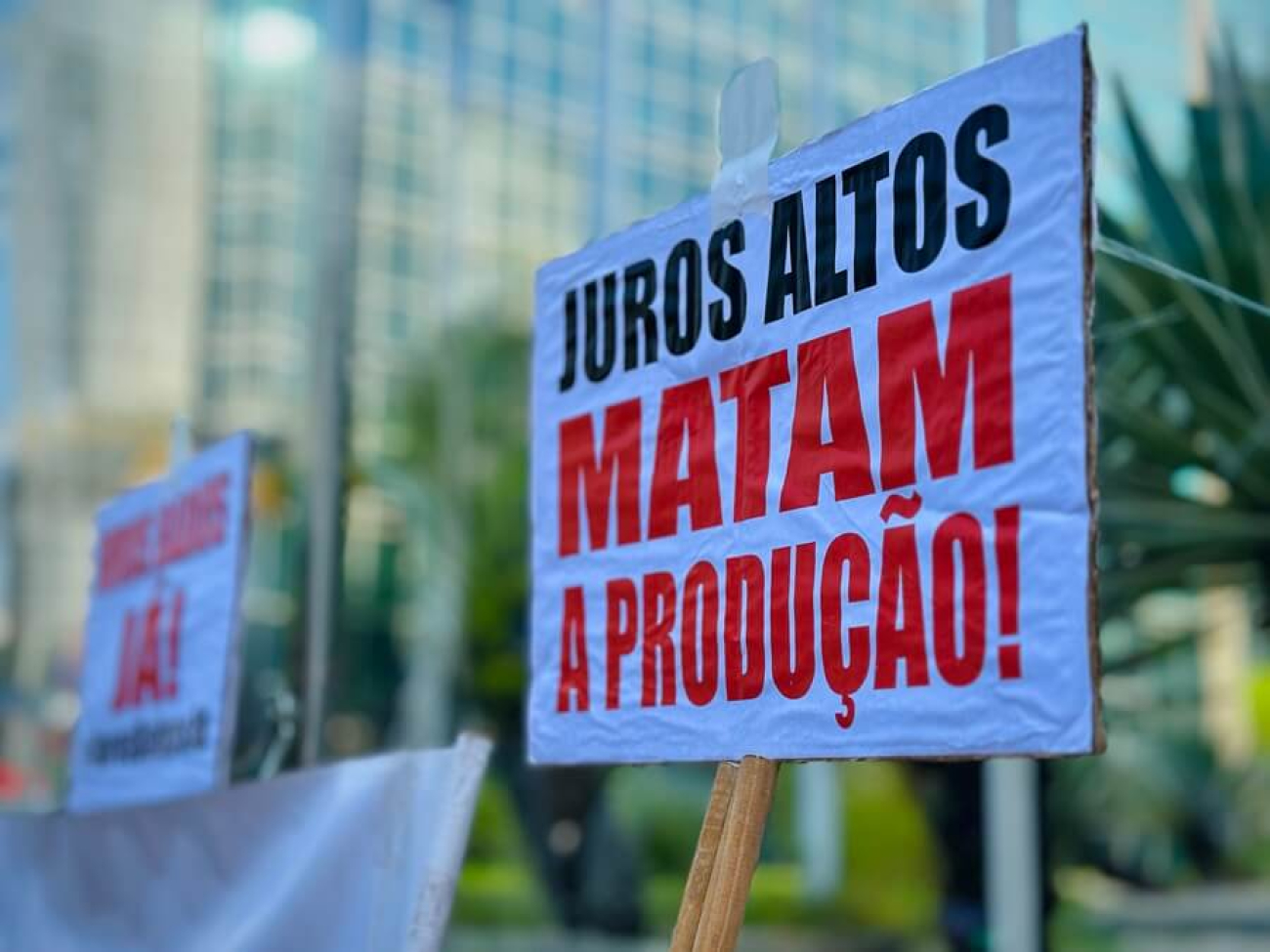 Imagem do ato contra a taxa selic, relizado pleos trabalhadores, mostra placa onde se lê "juros altos matam a  população"