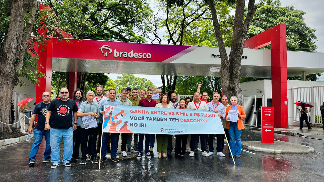 Cerca de 20 dirigentes posam em frente à entrada da Cidade de Deus, matriz do Bradesco, segurando faixa que anuncia isenção do IR para queem ganha até R$ 5 mil e descontos menores para quem ganha R$ 7.350