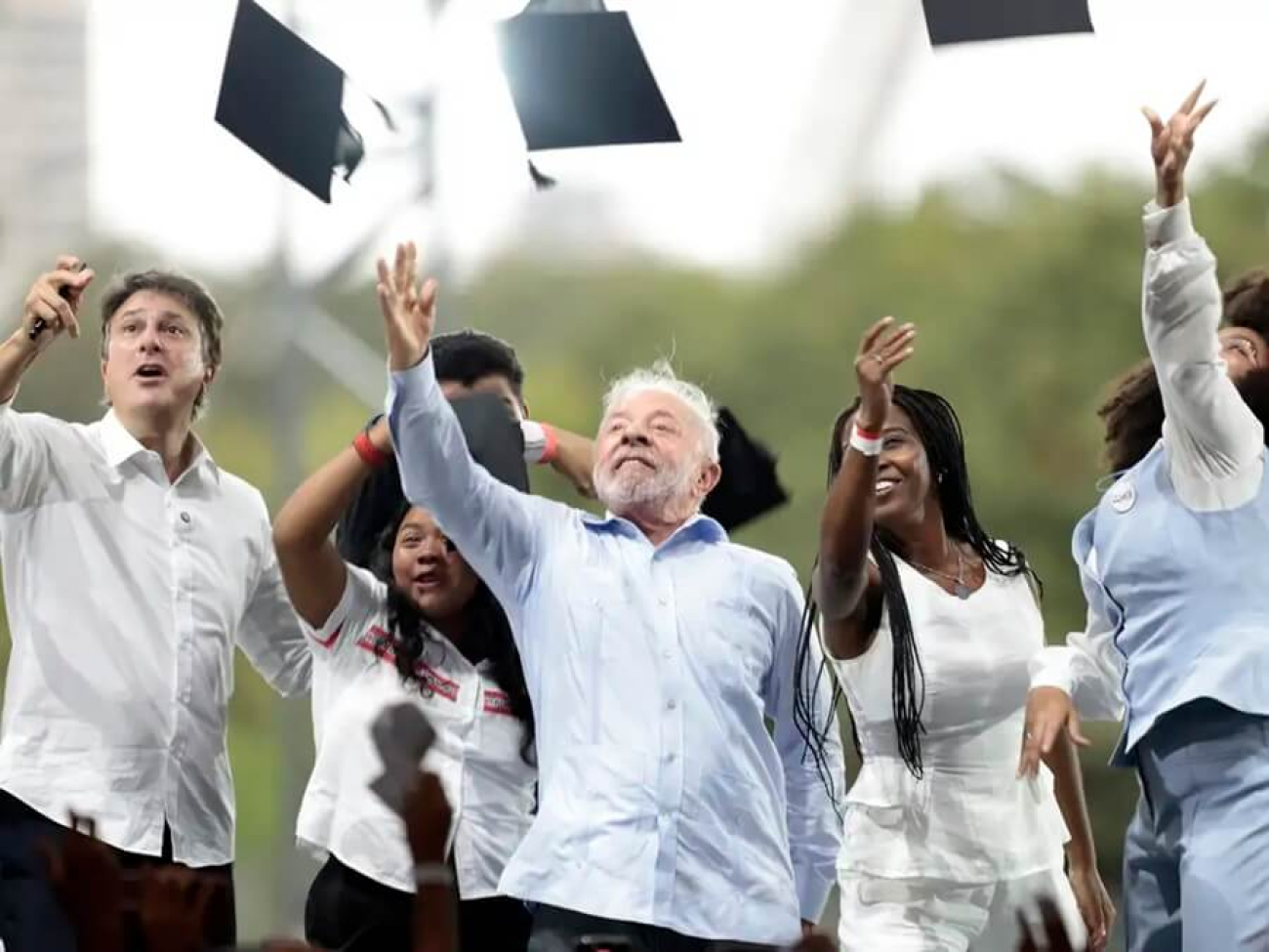 Imagem mostra Lula ao lado de esatudantes enquanto jogam capelos para cima