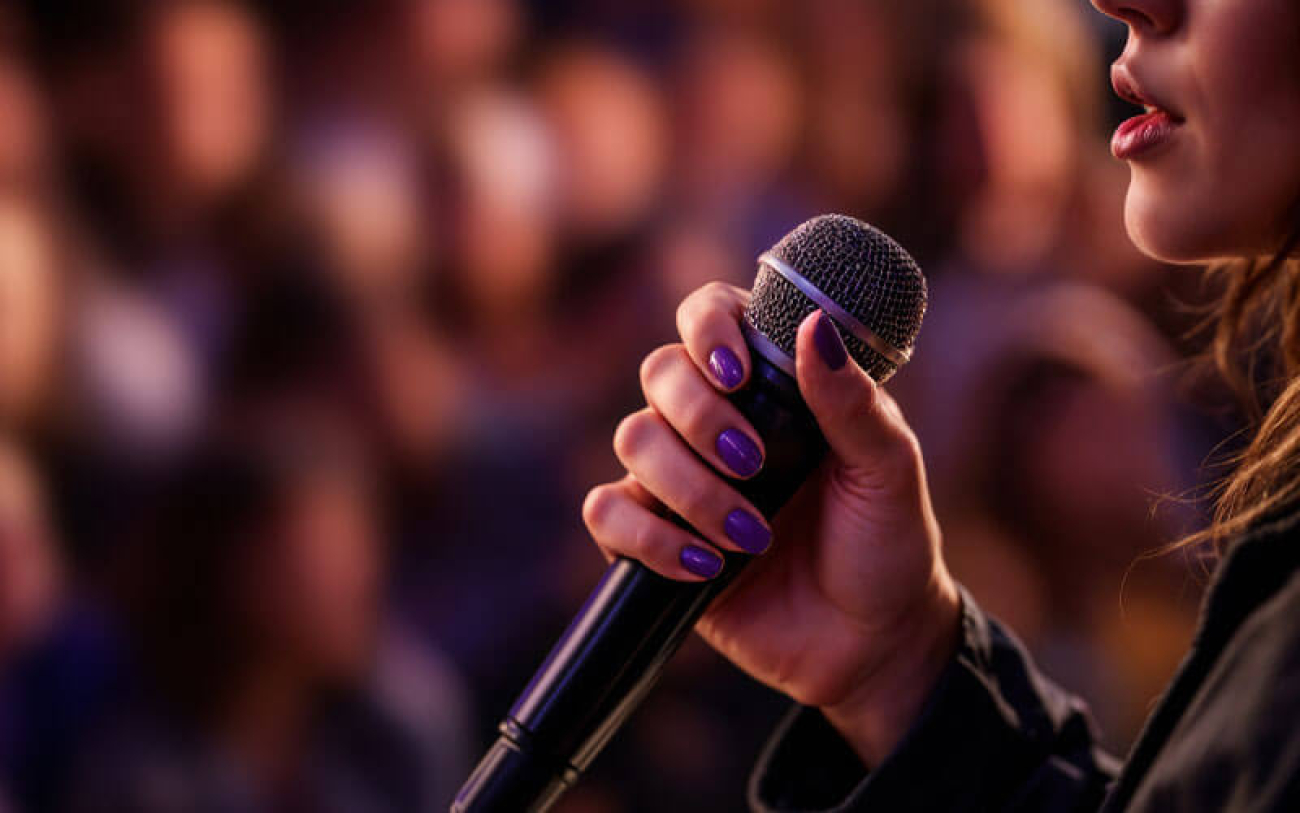 Perfil de uma mulher falando ao microfone em um auditório lotado