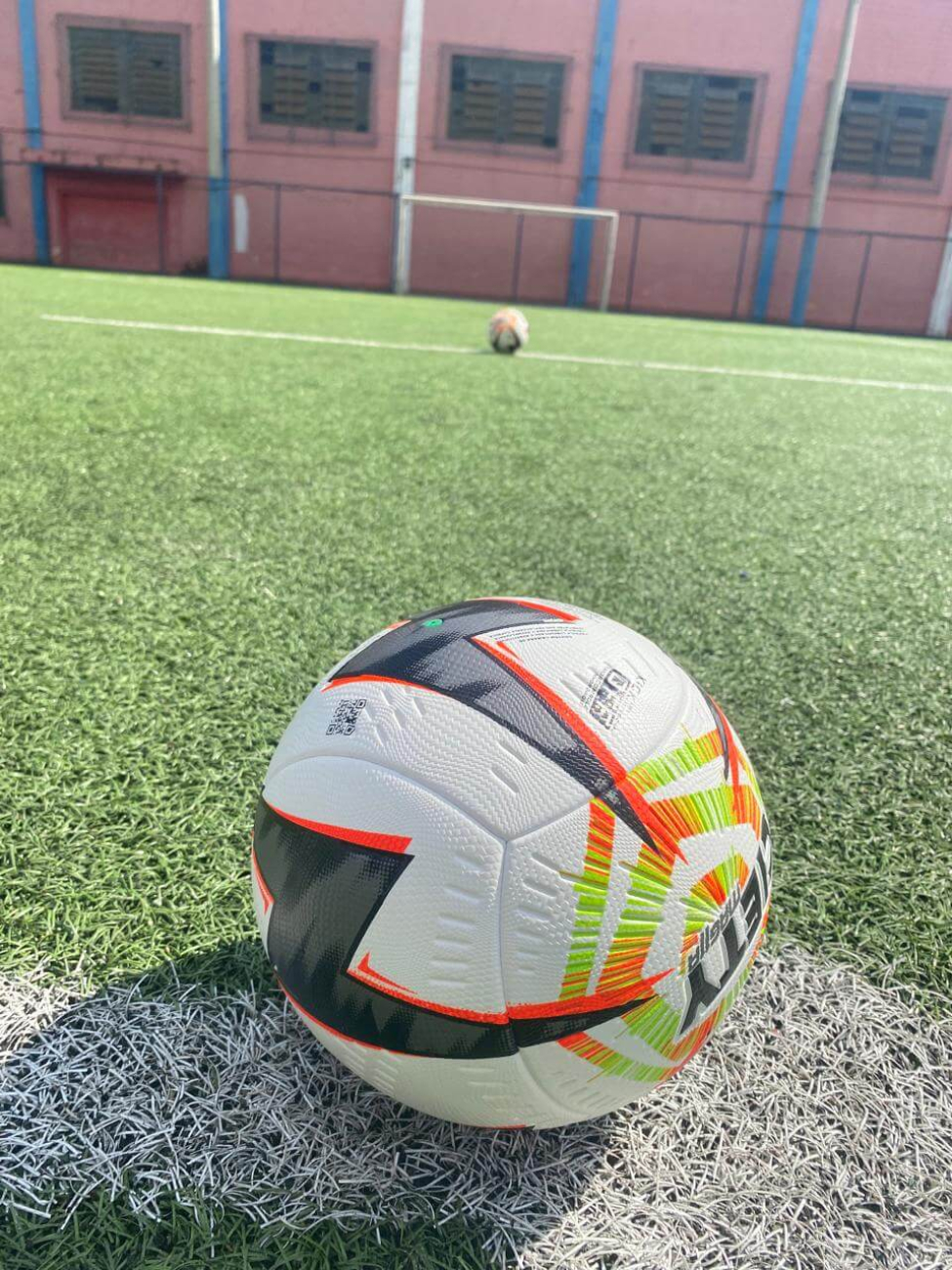 Campo de futebol com uma bola Penalty Mag11a F2 centralizada. Ao fundo as dependências do estádio Nicolau Alayon.