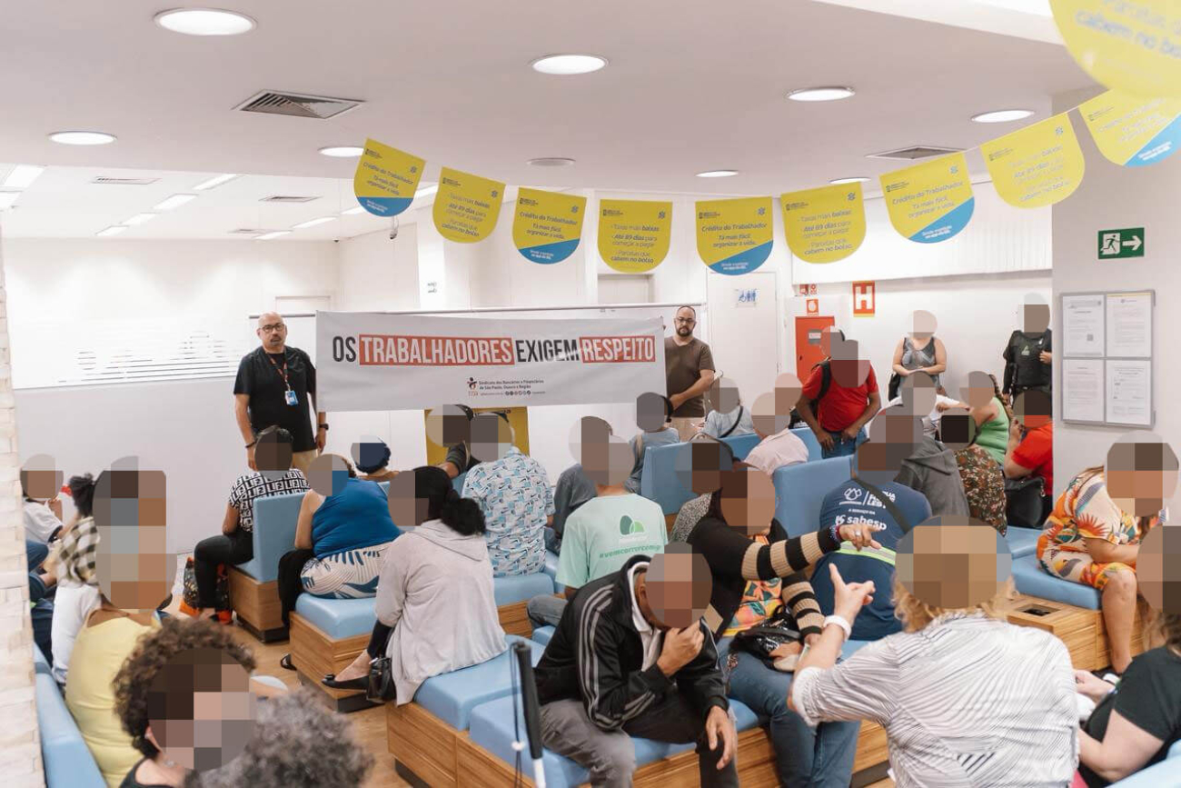 Imagem mostra dirigente do sindicato estendendo faixa onde se lê "os trabalhadores exigem respeito" dentro de uma agência superlotada do Banco do Brasil