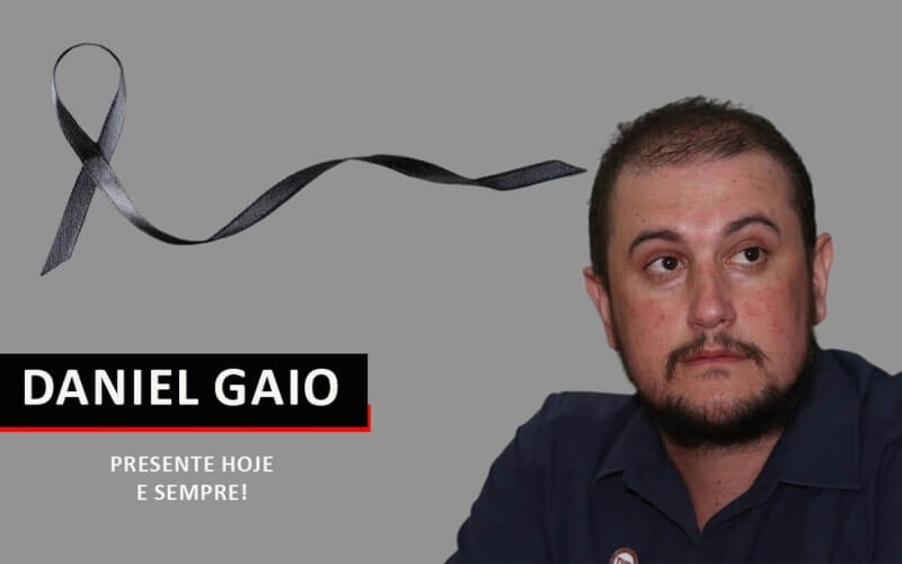 Homem moreno, cabelos pretos e curtinhos com camisa preta em fundo cinza