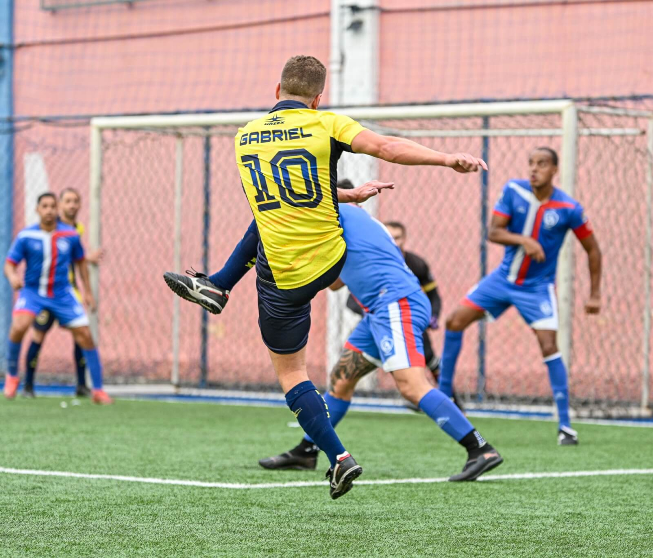 Jogador vestindo a camiseta do Equador chutando uma bola contra 3 adversários de azul