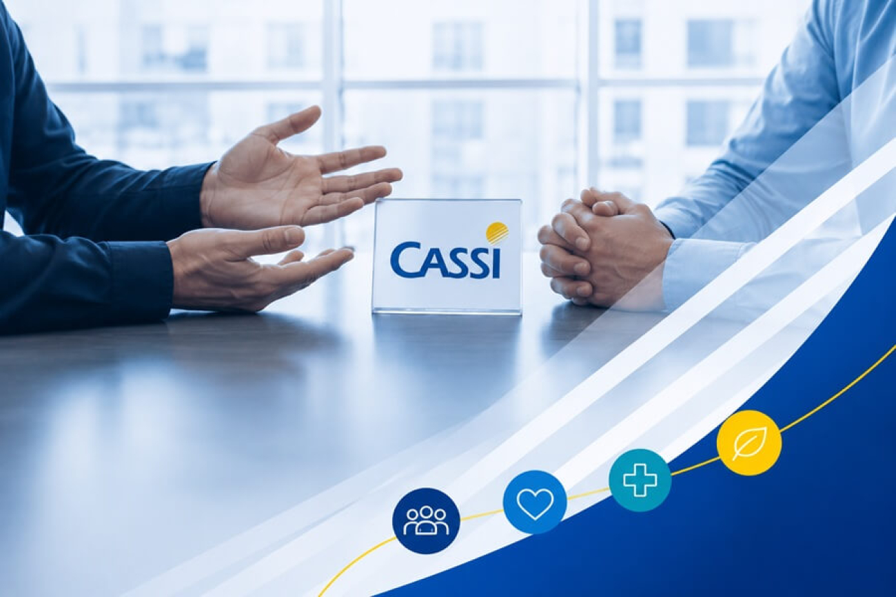 Imagem composta de uma foto que mostra mãos de duas pessoas frente a frente em uma mesa de negociação. entre eles e sobre a mesa há uma placa com o logo da Cassi. No canto inferior direito há ícones remetendo à saúde, como um coração e uma cruz