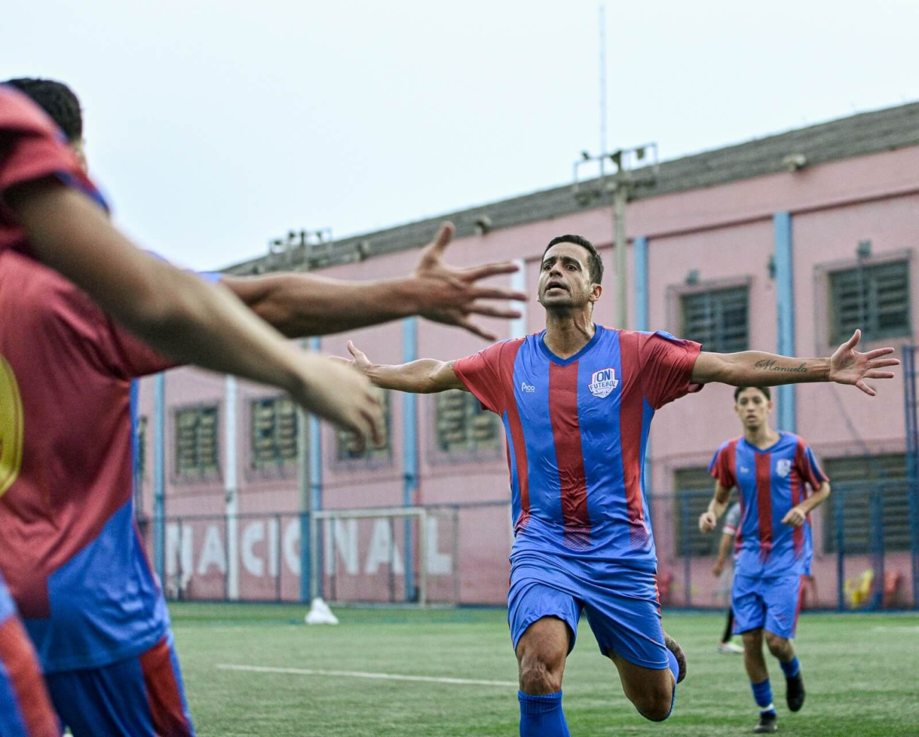 Jogador de futebol após marcar um gol correndo para receber o abraço dos companheiros.