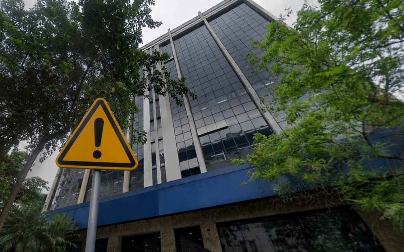 Imagem mostra fachada do prédio são joaquim da caixa econômica federal. em frente ao prédio há uma placa com um ponto de exclamação dentro de um triângulo amarelo com linhas negras seguindo paralelamente os lados da figura geométrica. a placa é o sinal universal para indicar perigo