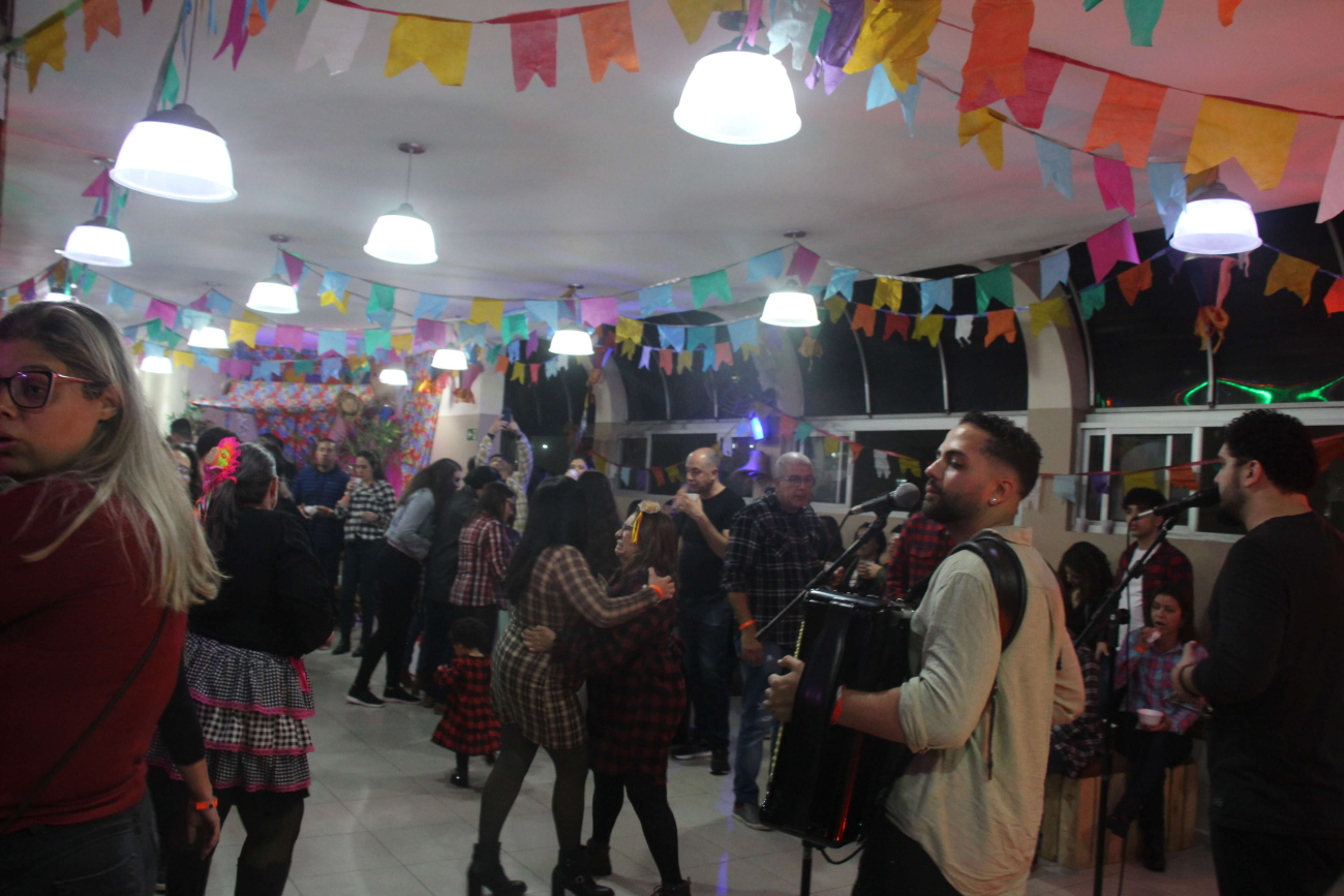Imagens do Arraiá dos Bancários, na imagem, um salão cheio com pessoas com roupa tradicional junina dançando músicas típicas.