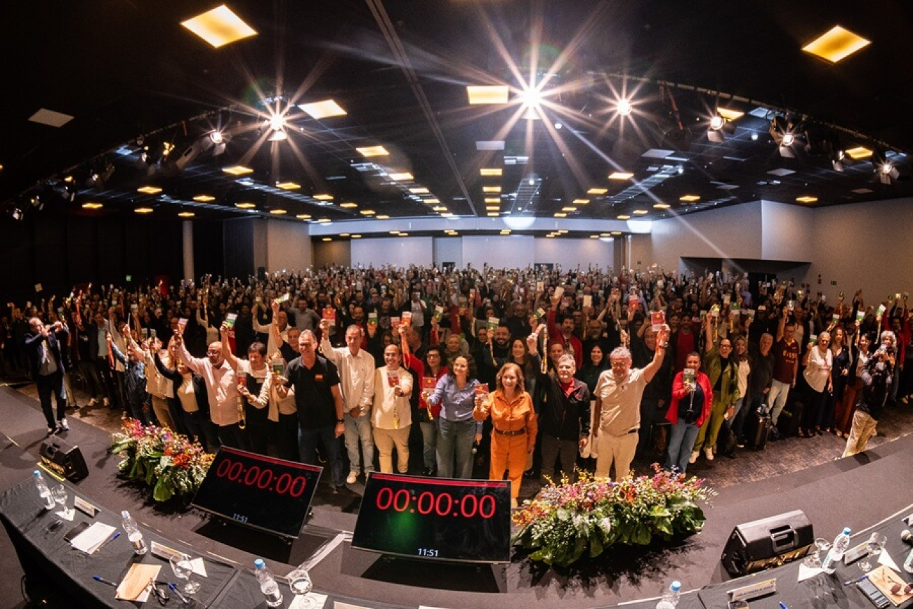 Imagem mostra auditório lotado de bancários com os braços erguidos durante a conferência nacional dos bancários