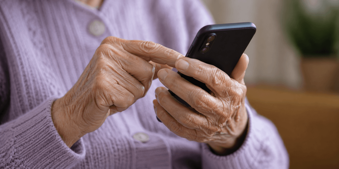 Imagem das mãos de uma mulher idosa teclando em um celular