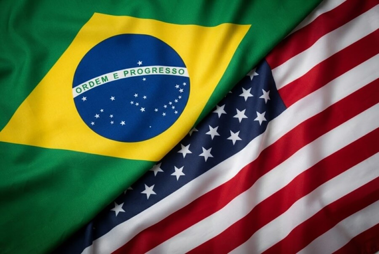 Imagem dividida ao meio, com a linha divisória diagonal, do canto superior direito ao canto inferior esquerdo. Na parte de cima, há a bandeira do Brasil. Na parte de baixo há bandeira dos Estados Unidos