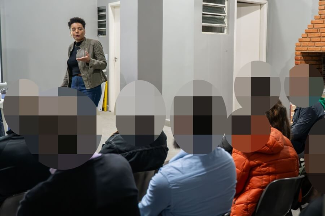 Imagem mostra a dirigente susana malu córdoba falando a bancários durante plenária. Ela está em pé em, um tablado, em frente aos bancários, que estão sentados. Susana é uma mulher negra, de cabelos curtos na faixa dos 35 anos