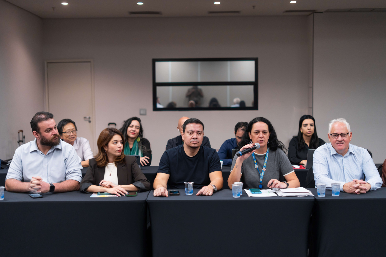 Foto dos representantes dos empregos da Caixa na mesa de negociação com o banco desta quarta (19); ao microfone, a diretora do Sindicato, Luiza Hansen