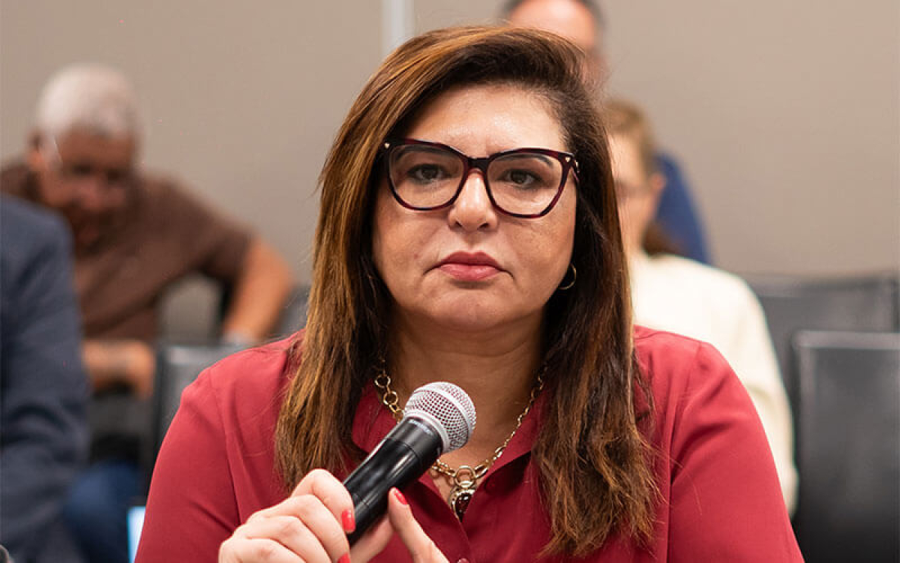 Foto da presidenta do Sindicato dos Bancários de São Paulo, Neiva Ribeiro, com uma camisa vermelho, segurando o microfone, na mesa de negociação com a Fenaban