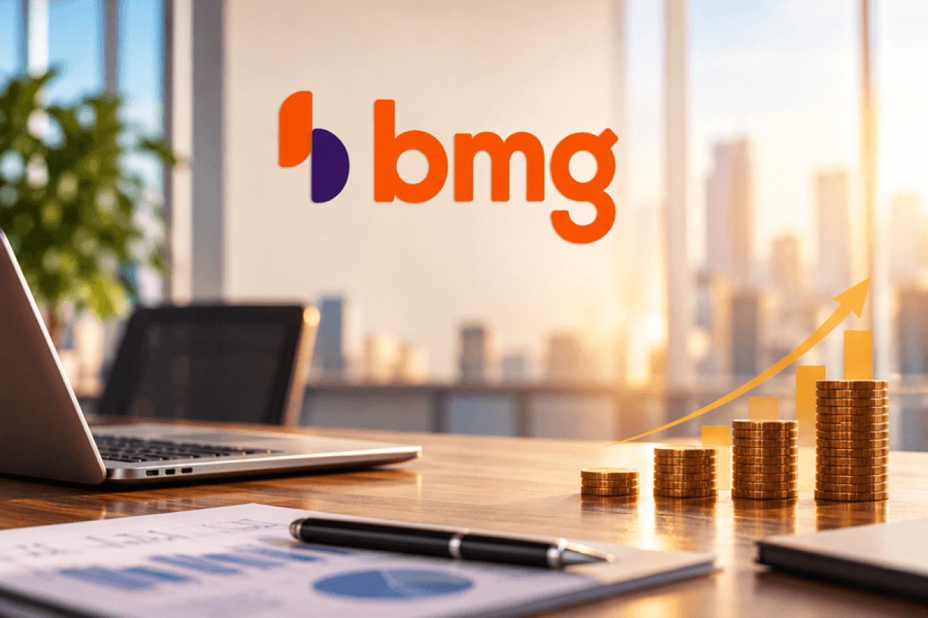 Imagem ilustrativa do PPR 2026 do Banco BMG, com logotipo do banco ao fundo e, sobre uma mesa de escritório, notebook, gráficos financeiros e pilhas de moedas em ordem crescente, simbolizando a participação nos resultados.