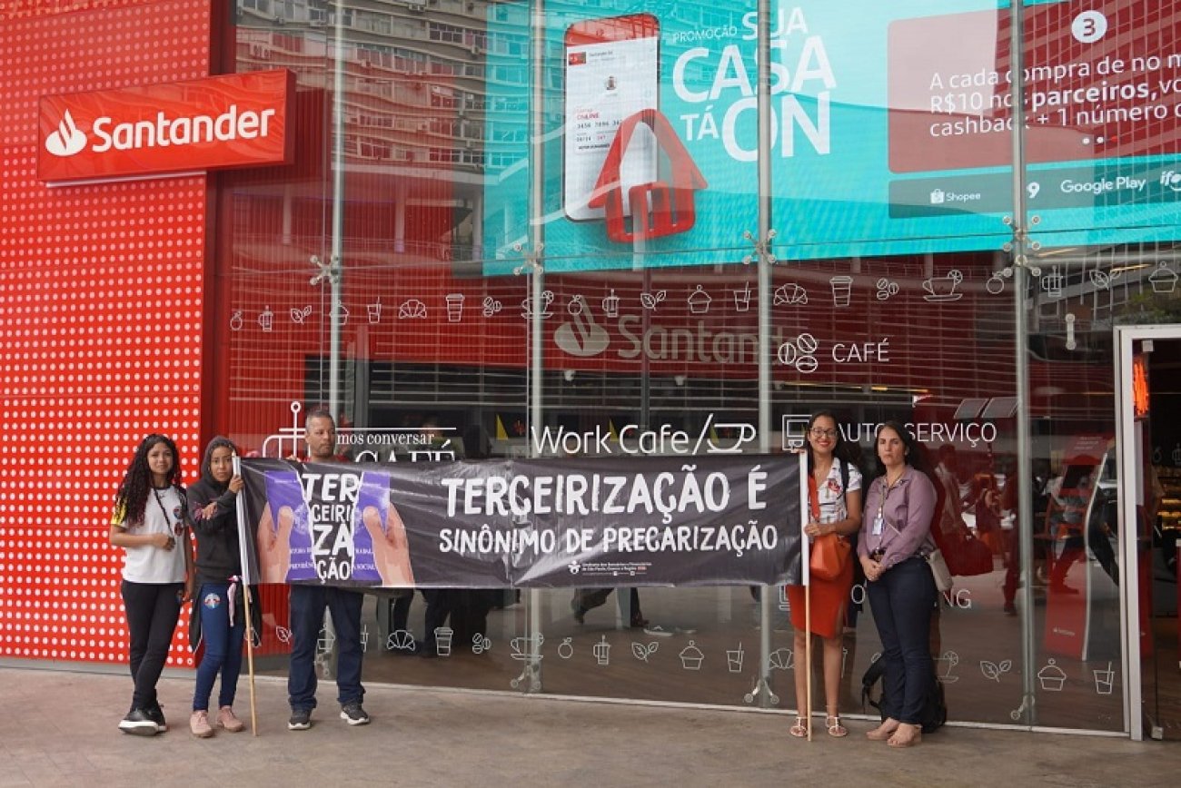 Dirigentes sindicais protestam contra terceirizações no Santander, na avenida Paulista. Eles estão em frente a uma agência e seguram uma faixa escrita "terceirização é sinônimo de precarização"