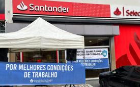 Imagem mostra fachada de uma agência do Santander. Em frente a ela está estendida uma faixa onde se lê "por melhores condições de trabalho"