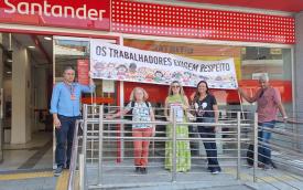Foto onde se vê um grupo de cinco dirigentes sindicais bancários em frente a uma agência do Santander, segurando uma faixa com a frase: Os trabalhadores exigem respeito